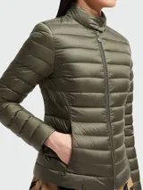 Chaqueta acolchada ligera color rosa pálido, con cuello alto y cierre frontal de cremallera. Presenta costuras horizontales y un calce ajustado.