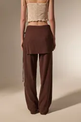 Pantalon de corte recto y tiro alto, confeccionado en tela texturizada color marrón, con detalle de falda superpuesta en la cintura.