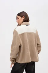 Campera de sherpa doble faz en color crema con detalles en verde oliva. Presenta cierre frontal con botones, bolsillos laterales de nylon capitoneado y terminaciones en contratono. Diseño de calce relajado con bordado en la manga.