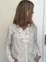 Camisa de lino con estampado floral en tonos pasteles, cuello camisero, mangas largas y detalles de jabot y encaje en puños y pechera.