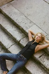 Top chaleco negro satinado con cuello halter, espalda descubierta y cierre frontal con cremallera y botón a presión ocultos por solapa.