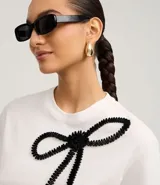 Remera blanca de algodón con cuello redondo, mangas cortas y bordado de lazo negro en la parte delantera.