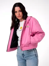 Chaqueta corta de lona color rosa, con capucha ajustable, cierre frontal y forro interior acolchado negro. Presenta un parche con el logo de la marca en el pecho.