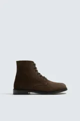 Bota tipo derby con cordones, confeccionada en piel con acabado de serraje. Presenta horma cuadrada y suela con ligero tacón.