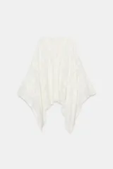 Blusa tipo capa de algodón con escote en pico y cierre frontal con botones. Presenta mangas largas amplias y diseño con bordados florales a tono, con bajo asimétrico.