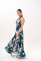 Vestido largo con escote halter profundo y diseño sin mangas. Presenta un estampado difuminado en tonos azules, celestes, blancos y grises, con corte ajustado en el torso y una falda larga con vuelo.