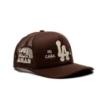 Gorro trucker marrón con diseño de red en la parte trasera, visera curva y bordado frontal en relieve color beige con letras "LA" y el texto "Mi Casa Su Casa".