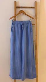 Pantalón de corte ancho y relajado, confeccionado en lino con diseño de rayas verticales. Presenta cintura elástica con cordón de ajuste y bolsillos laterales.