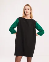 Vestido corto negro con mangas 3/4 verdes, cuello bote y bolsillos laterales.