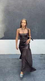 Vestido largo de diseño combinado, con cuerpo superior ajustado de efecto cuero en color chocolate y falda inferior fluida de gasa semitransparente. Presenta escote recto con breteles finos.