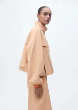 Chaqueta oversize de lyocell color beige, con cuello alto, cierre frontal oculto con botones y cremallera, bolsillos de solapa en el pecho, mangas largas con puños elásticos y bajo fruncido.