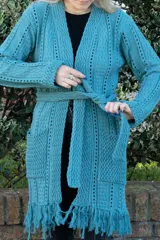 Sacón largo de tejido de punto calado color petróleo, con mangas largas y bolsillos delanteros. Presenta detalle de flecos en el ruedo.