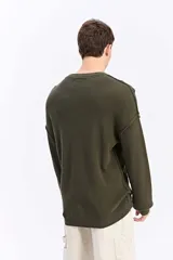 Sweater oversize de tejido liviano color gris claro, con hombros caídos, cuello redondo, costuras a la vista y bordado sutil en el pecho.