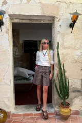 Blusa negra de manga 3/4 con cuello alto, confeccionada en algodón con paneles horizontales de encaje negro en el torso. Presenta un fajín integrado que se anuda a la cintura y puños con volado de encaje.