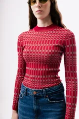 Top de punto ajustado al cuerpo, con cuello redondo y manga larga. Presenta un diseño de estampado geométrico a cuadros en tonos rojos y rosados.