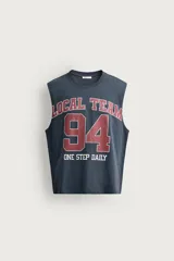 Musculosa gris oscuro de ajuste relaxed, con cuello redondo y diseño sin mangas con sisa amplia. En el frente presenta una estampa estilo varsity en tonos bordó y blanco con la inscripción "Local Team 94 One Step Daily".