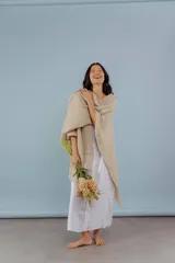 Ruana tejida a mano en lana merino color beige, con textura de punto y detalle de flecos en el ruedo. Presenta sutiles destellos brillantes integrados en el tejido.