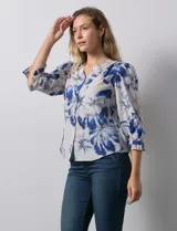 Blusa de gasa estampada con flores azules y blancas, marca Sioni. Tiene escote en V, abertura frontal con botones y mangas 3/4 con puños fruncidos y botón.