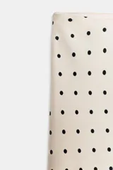 Falda midi de tejido satinado con estampado de lunares negros sobre fondo beige. Presenta un diseño de tiro medio con cintura elástica y un bajo con corte asimétrico.