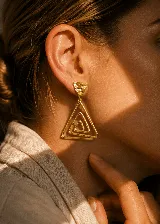 Aros colgantes dorados con diseño geométrico de triángulos concéntricos y pieza superior con textura irregular.