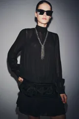 Vestido corto de viscosa color negro con cuello perkins y manga larga. Presenta un fajín de terciopelo integrado con bordados a tono y detalle de lazadas laterales.
