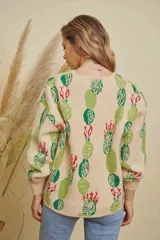 Buzo tejido de punto con diseño estampado de cactus en tonos verdes y rojos sobre base color crema. Presenta cuello redondo y mangas largas con puños acanalados.