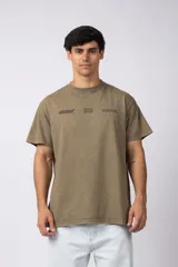 Remera color verde oliva con cuello redondo y manga corta. Estampado en el pecho con la palabra "planet" en tipografía cursiva, un logo con forma de circuito y una hilera de cuadros blancos y negros.