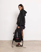 Mochila negra de tejido técnico resistente con gran capacidad (20L). Presenta un compartimento principal con cierre, funda interior y correas de hebilla de seguridad en el frente. El logo de Coolway está impreso verticalmente en blanco y en una etiqueta roja. Incluye bolsillos laterales de malla.