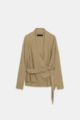 Chaqueta de punto de color tostado, con escote en V y manga larga. Diseño cruzado al frente con cinturón lazada en el mismo tejido y detalle de hebilla metálica circular en el lateral.