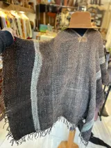 Poncho de lana virgen tejido en telar, de diseño tupido en tonos marrones con rayas anchas y flecos en el ruedo.