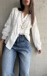 Camisa blanca de manga larga con detalles de encaje y diseño abotonado en la parte delantera.
