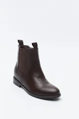 Bota tipo chelsea de caña media confeccionada en cuero sintético, con paneles laterales elásticos y presillas superiores. Presenta un diseño minimalista con suela plana y punta redondeada.