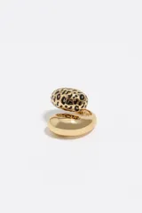 Anillo envolvente de latón con acabado dorado. Presenta un diseño asimétrico donde un extremo es liso y redondeado, mientras que el otro cuenta con un estampado de manchas tipo animal print realizado en esmalte negro.