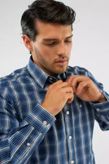 Camisa de manga larga con diseño de cuadros en tonos azules, blancos y negros. Presenta cuello clásico, cierre frontal con botones y logo bordado en el pecho. Corte semi slim.