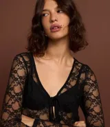 Blusa de manga larga confeccionada en encaje floral transparente, con escote en V y cierre frontal mediante lazos.