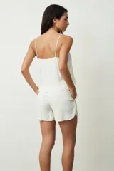 Musculosa color crudo con escote en V y botones frontales. Presenta un pequeño volante en el ruedo inferior.