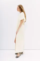 Vestido largo color crema, con escote en V en el frente y espalda. Presenta mangas cortas amplias, talle ajustado con lazo trenzado y tajos laterales.