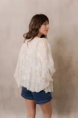 Kimono marfil de silueta amplia, confeccionado en tela con bordados florales y detalles calados. Cuenta con mangas amplias tres cuartos, frente abierto y terminaciones decorativas.