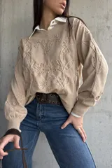 Sweater de punto color beige con diseño bordado en relieve de flores y hojas. Presenta cuello redondo, mangas largas con puños acanalados y un corte holgado.