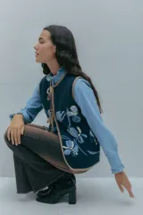 Chaleco de lana color rosa con bordados florales artesanales en tonos rosados y marrones. Presenta un diseño sin mangas con cierre frontal mediante lazos ajustables y terminaciones en color marrón.