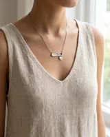 Collar de acero con cadena fina y dije compuesto por una barrita horizontal y un pequeño corazón colgante.