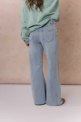 Pantalón de jean color arena con silueta wide leg, tiro medio-alto y costuras verticales delanteras que estilizan la figura. Cuenta con bolsillos funcionales y cierre frontal con doble botón.