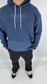 Canguro azul con capucha, corte oversize y estampado en el frente con la leyenda "Duxon Co." en letras mayúsculas, seguido de texto en japonés y la palabra "Tokyo".