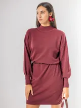 Vestido tipo polerón de tejido de punto color borgoña, con cuello alto, mangas largas con puños ajustados y corte recto. Incluye un cinturón del mismo material con una hebilla decorativa de flor con cristales.