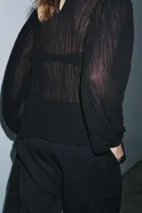 Blusa negra de manga larga abullonada, con tejido plisado y cuello redondo con abertura y botón en la espalda.
