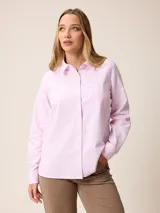 Camisa de manga larga con cuello clásico y cierre frontal de botones, confeccionada en tela de algodón con diseño de rayas verticales finas en color rosado y blanco. Presenta un bolsillo frontal en el pecho con detalle de etiqueta pequeña.