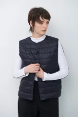 Chaleco acolchado tipo puffer, color beige, sin mangas, con cuello redondo y cierre frontal con botones a presión.