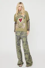Remera verde militar de manga corta, con cuello redondo y diseño holgado. Presenta una estampa frontal con la palabra "GYPSY", un corazón rojo rodeado de rayos y dos leopardos acompañados de detalles decorativos y tipografía estilo vintage.