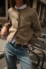 Chaqueta color tostado con efecto ante, cuello redondo y manga larga. Presenta detalles de acabados trenzados en el cuello, el cierre frontal, los puños y el bajo. Cuenta con cierre frontal de botones y bolsillos delanteros de vivo.