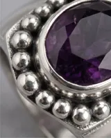 Anillo de plata 925 con piedra amatista central de corte circular, rodeada por un diseño de pequeñas esferas metálicas.